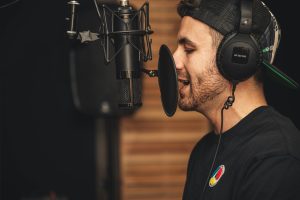 A young male musician singing in a professional recording studio with a microphone and headphones.