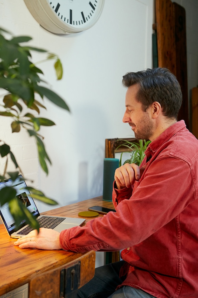 singing teacher sat sideways looking at macbook smiling