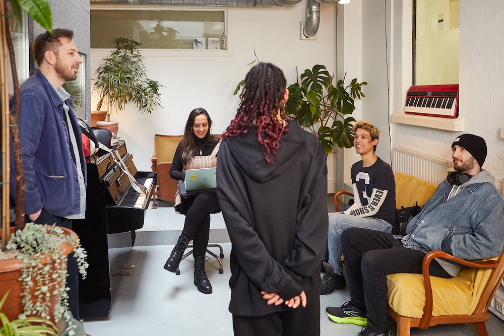 Group singing lesson in progress in modern studio with plants and lights, piano and keyboard