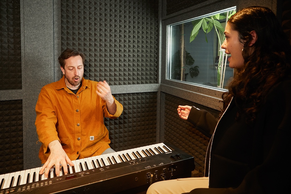 singing teacher playing keyboard in a sound booth with student singing