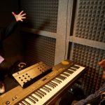 singing teacher playing keyboard in a sound booth with student singing