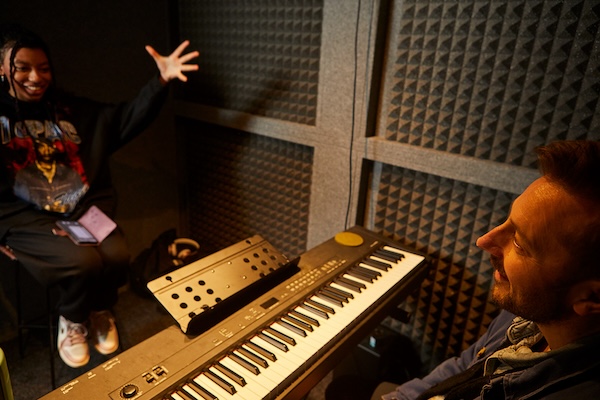 singing teacher playing keyboard in a sound booth with student singing
