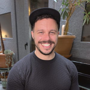 Mike Dzyngel, vocal coach at City Vocal Coach, smiling and wearing a black cap