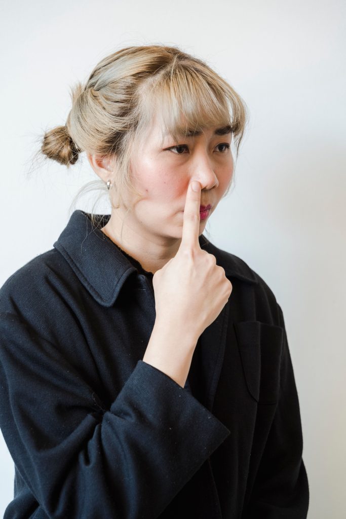 Asian woman in black jacket making a silly face with finger on nose against a white background.
