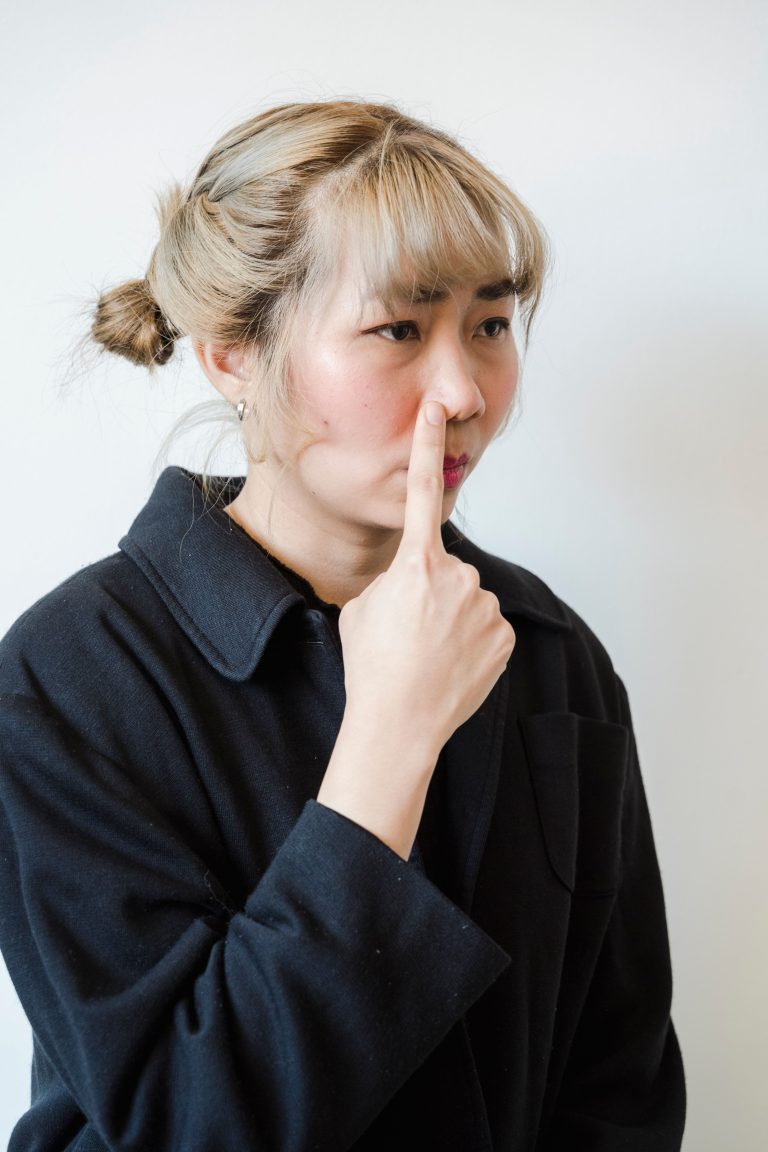 Asian woman in black jacket making a silly face with finger on nose against a white background.