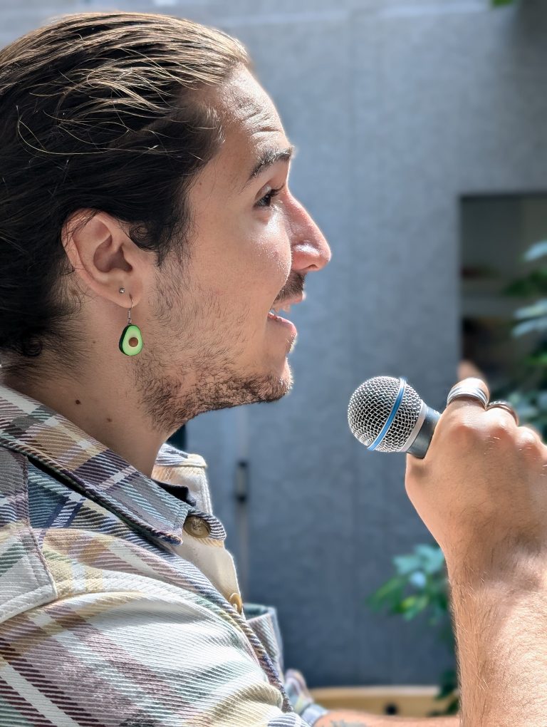 Man with shoulder-length hair singing into a handheld microphone, captured mid-phrase in a relaxed, natural moment