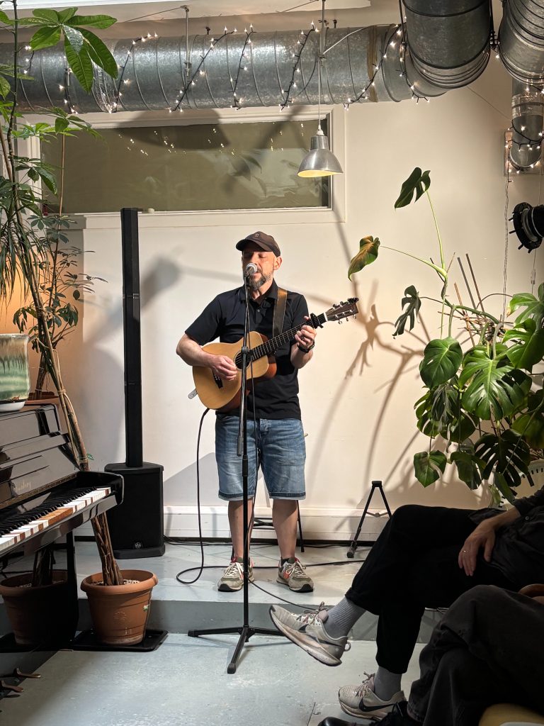 man with a guitar singing in a plant filled studio