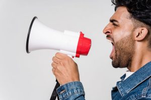 Close-up side view of a man shouting passionately into a megaphone, expressing urgency.